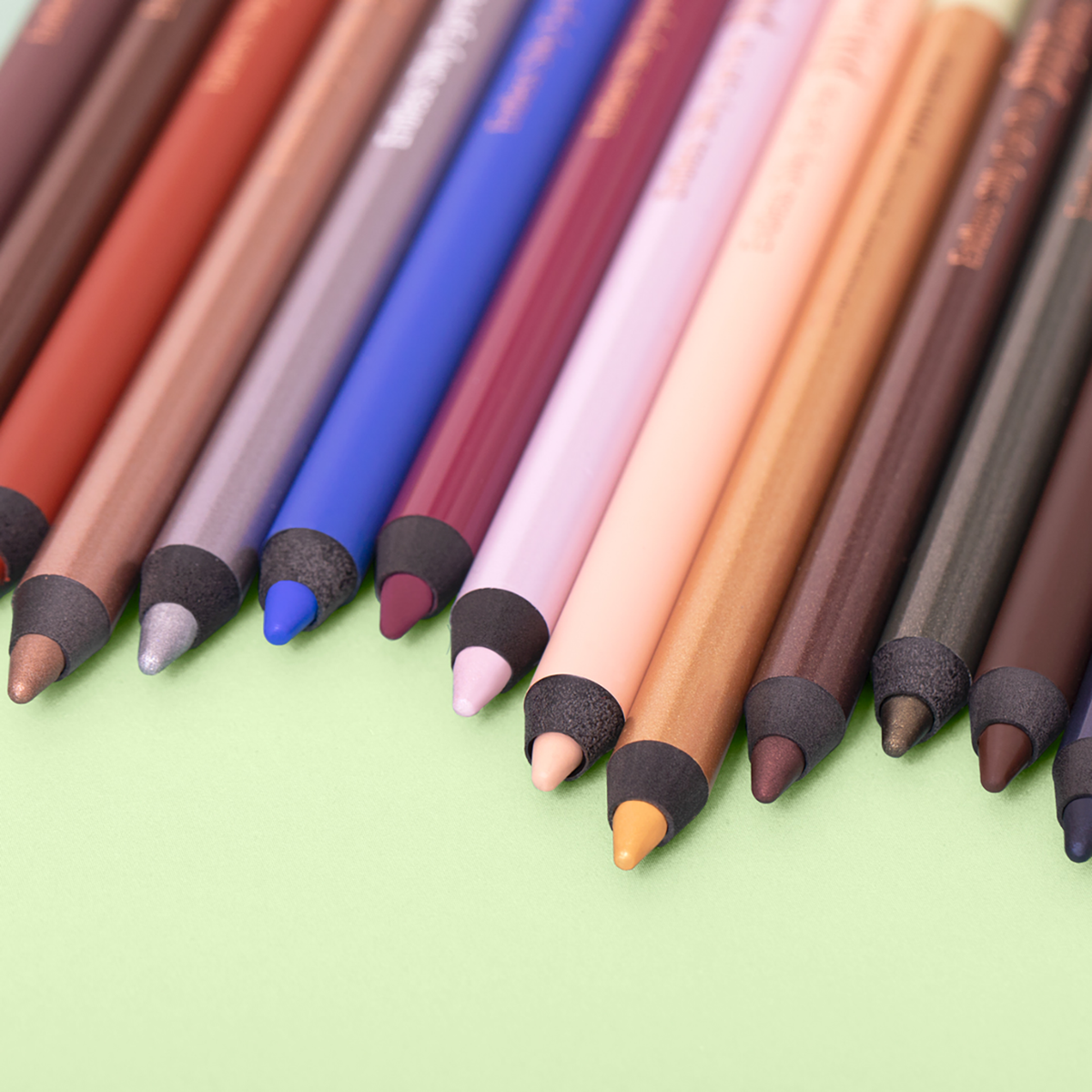 A collection of various colored eye liners, arranged side by side on a green background.