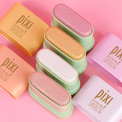 Six Pixi contour and highlight sticks in pastel shades of orange, peach, pink, mint green, white, and lavender, arranged diagonally on a solid pink background.