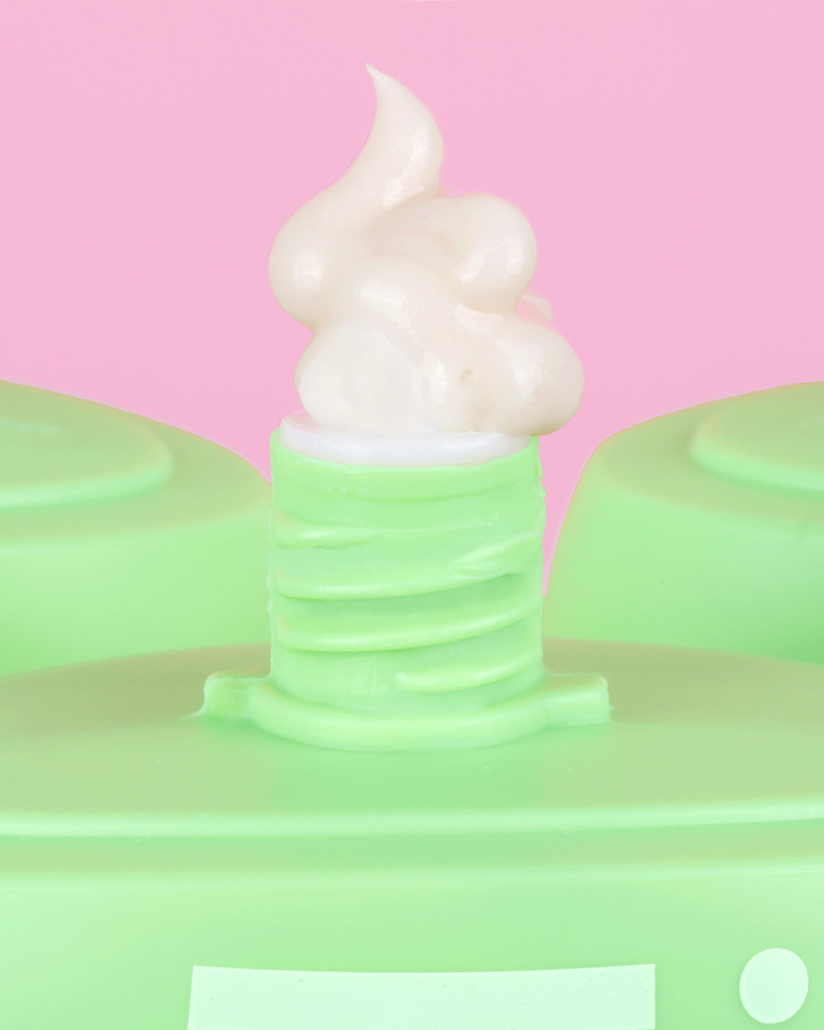 A close-up of Pixi HandHero dispensing a swirl of cream against a solid pink background.
