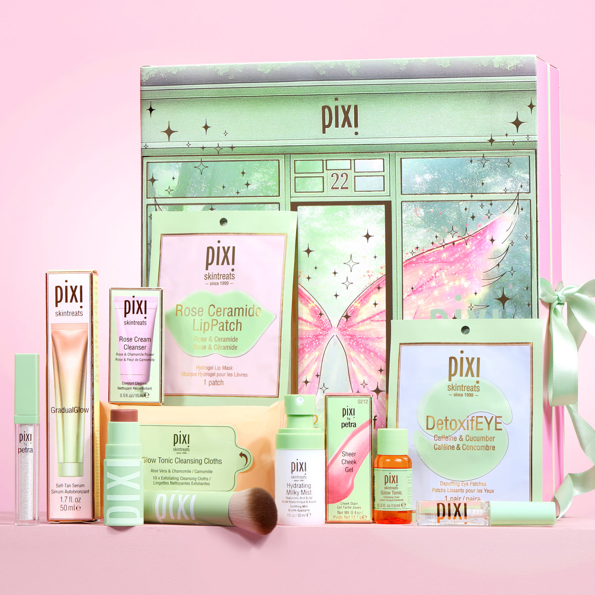 Pixi Beauty 12 Days of Discovery Advent Calendar gift set featuring a pastel green advent calendar box with fairy artwork, surrounded by skincare products including a lip patch, cleanser, toner, eye cream, and moisturizer on a pink background.