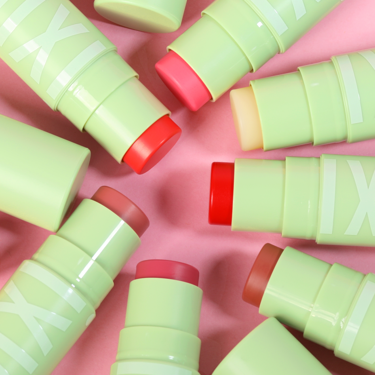 Green and red cosmetic sticks scattered on a pink background