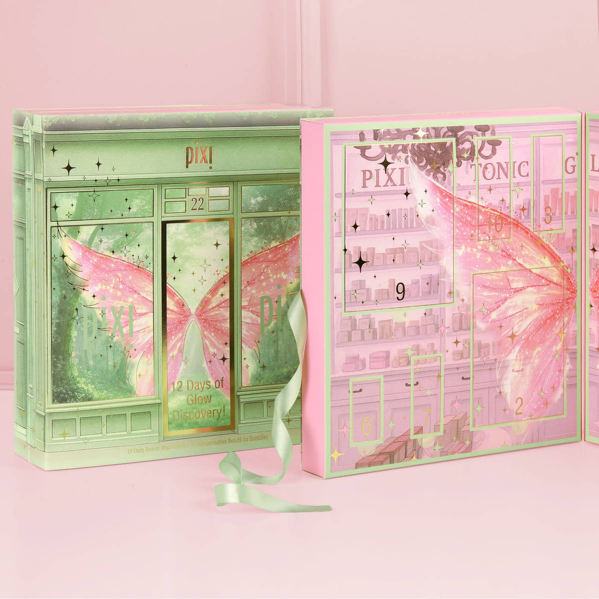 A Pixi advent calendar set styled like a fairy boutique, featuring a mint green storefront box with pink wings and a pink interior panel showing numbered compartments and cosmetic illustrations, with a pale green ribbon on a pink background.
